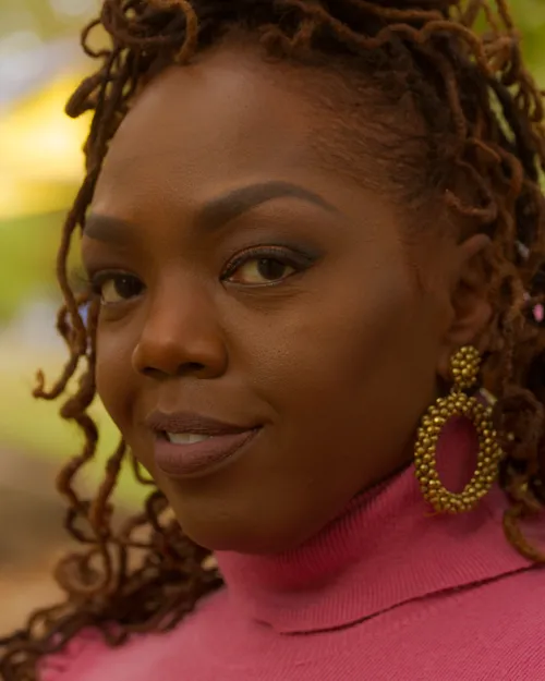 Close-up of Antoinique smiling softly, wearing a pink turtleneck and a gold beaded hoop earring.